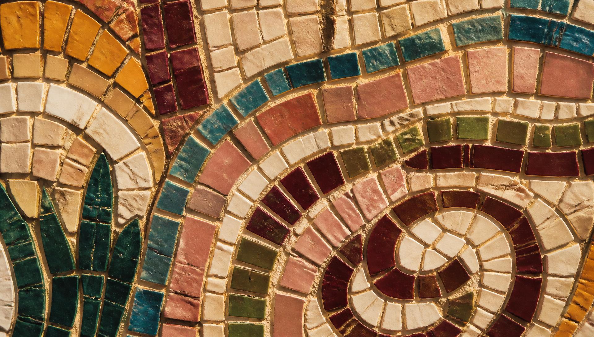 Full-width close crop of a hand-set mosaic panel in burgundy, olive, pink and ochre